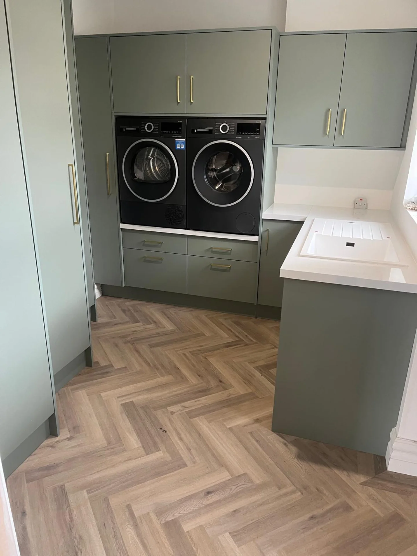 Sage utility laundry cabinetry with integrated appliances and storage.