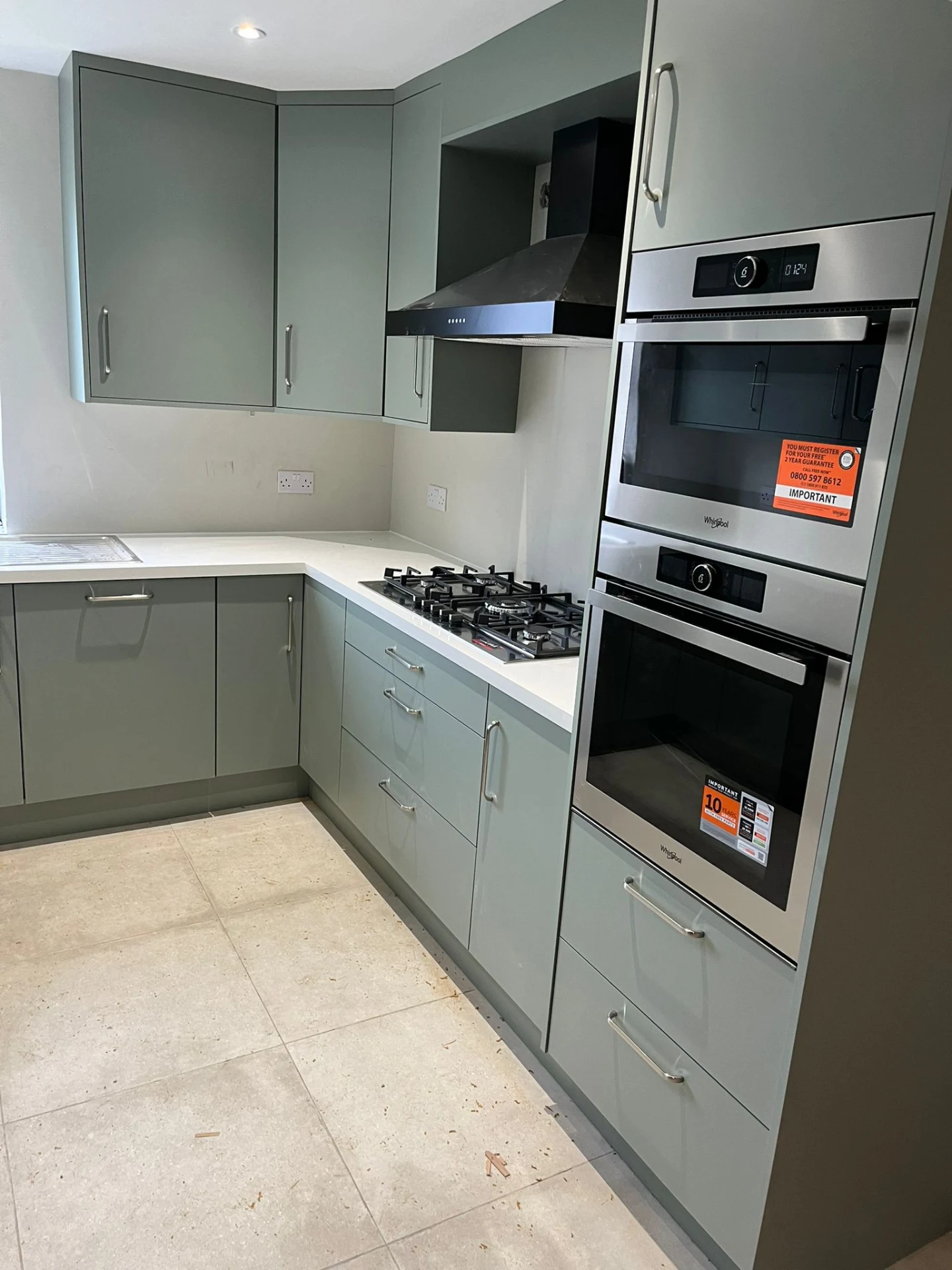Sage green compact kitchen with integrated appliance wall and clean worktop run.