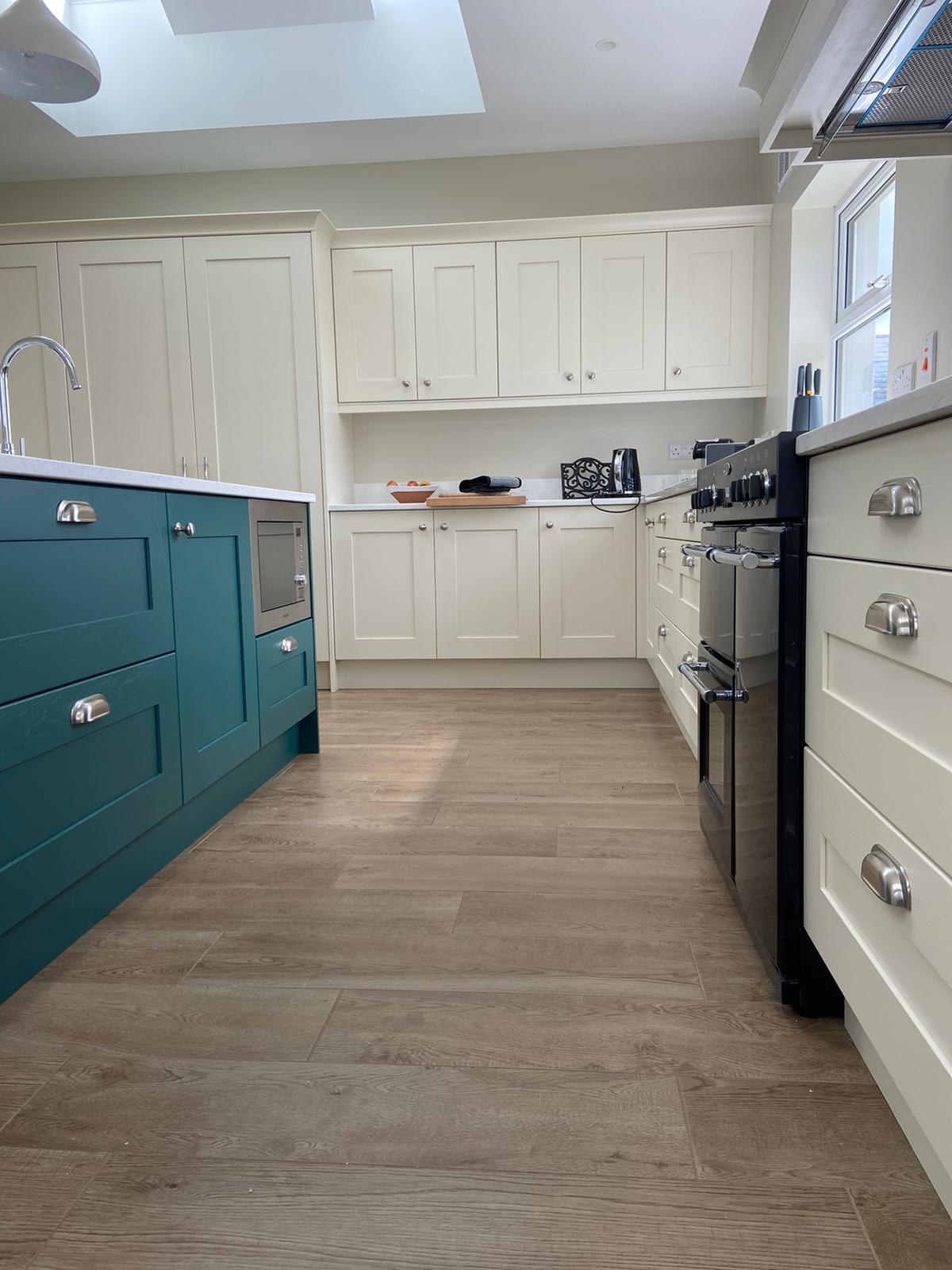Teal kitchen island with cream fitted cabinetry, oak flooring and a traditional range cooker.